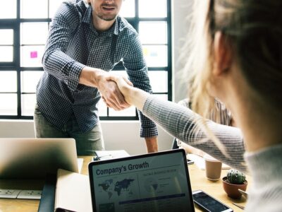 Two people shaking hands in front of a laptop.