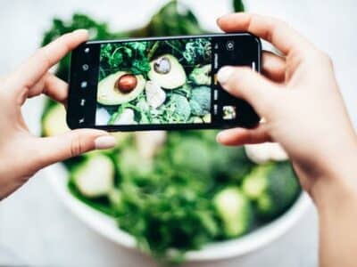 A person taking a picture of a bowl of vegetables with a smartphone.