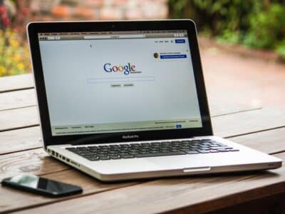 A laptop is sitting on a wooden table next to a cell phone.