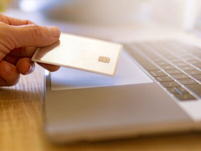 A person holding a credit card in front of a laptop.