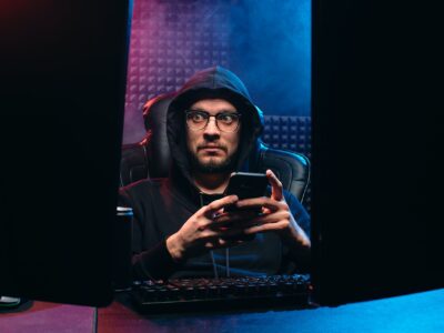 A man in a hoodie is using a cell phone in a dark room.