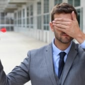 A businessman covering his eyes and holding a dart.
