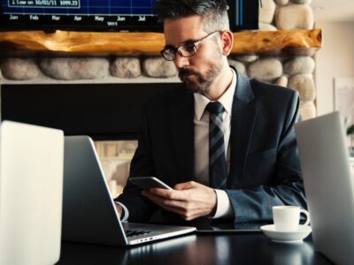 A businessman sitting at a desk with a laptop and cell phone.