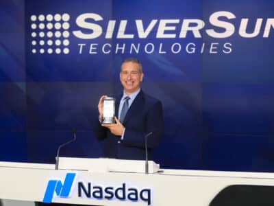 A man holding a silver sun technologies phone in front of a nasdaq sign.