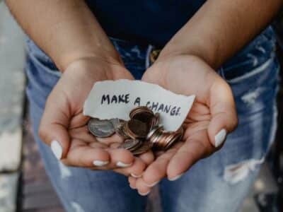 A woman's hands holding coins and a note that says make a difference.