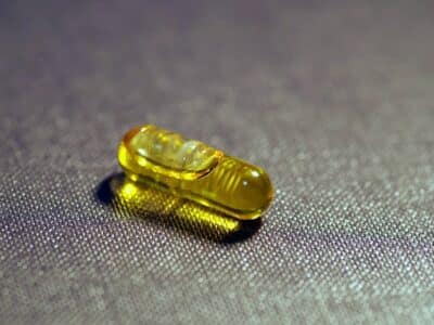 A small yellow pill sitting on a dark surface.