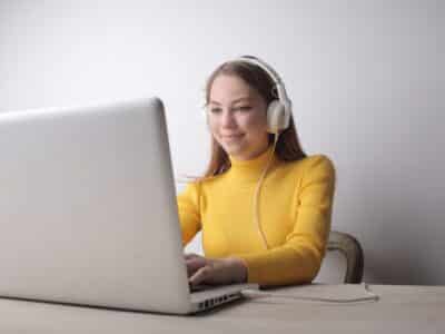 A young woman wearing headphones is using a laptop computer.