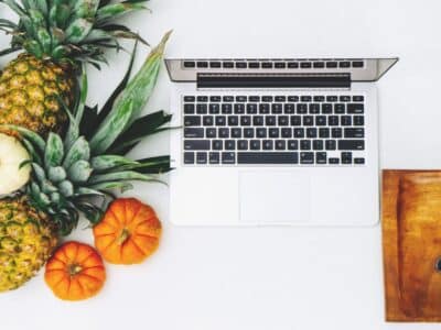 A laptop sits next to pineapples and oranges.