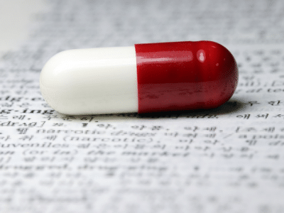 A red and white pill sitting on top of a dictionary.