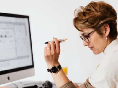 A woman looking at a computer screen with a pen.