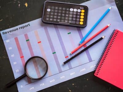 A notebook, calculator, pen and magnifying glass on a table.