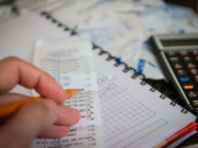 A person writing on a notebook with a pencil and a calculator.