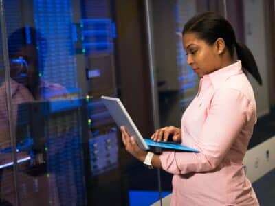 A woman using a laptop in a server room.