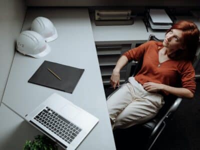 A woman in a hard hat sitting at a desk with a laptop.