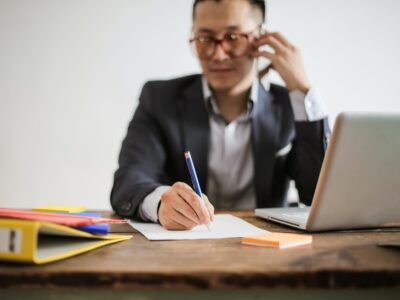 A man in a suit sitting at a desk with a pen and notebook.