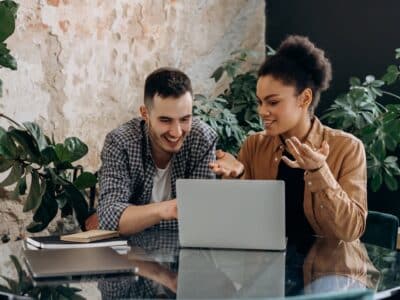 Two people sitting at a table looking at a laptop.