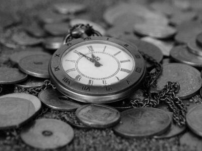 A black and white photo of a pocket watch laying on a pile of coins.