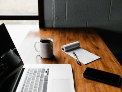 A laptop sits on a wooden desk next to a cup of coffee.