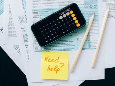 smartphone over tax forms with post-it note - this list of Sage 100 year-end resources will help you close out 2023