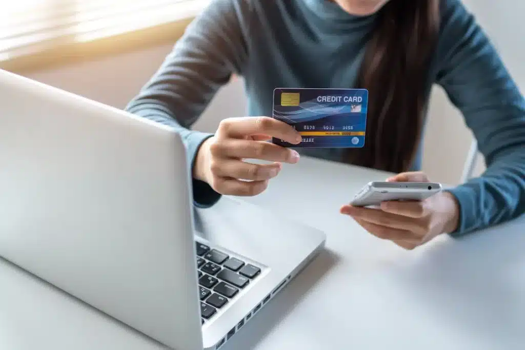 person holding a credit card and phone next to a laptop; example of how Acumatica ERP can help integrate with ecommerce software