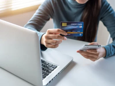 person holding a credit card and phone next to a laptop; example of how Acumatica ERP can help integrate with ecommerce software