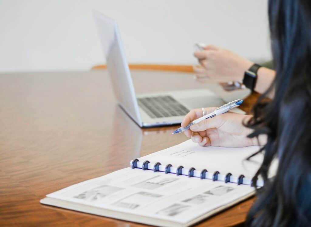 A woman writing in a notebook on a table while her coworker uses a laptop at a small business using Sage 50