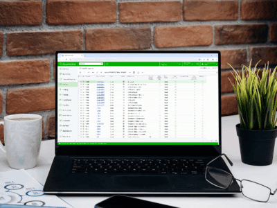 Black laptop displaying Acumatica General Ledger journal transactions screen on a desk with coffee mug and notepad, showcasing the financial management interface on a computer in an office setting.