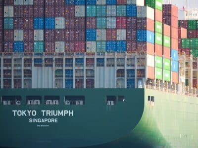 Cargo ship "Tokyo Triumph" loaded with shipping containers in various colors, representing international trade and supply chains affected by tariffs impacting manufacturing operations.