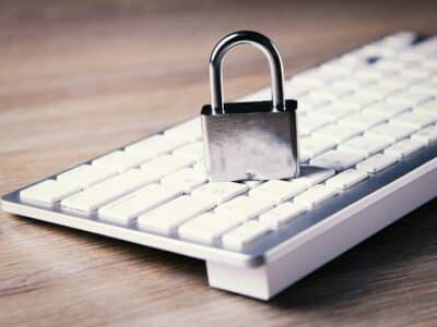 Silver padlock sitting on white computer keyboard on wooden desk, symbolizing cybersecurity and data protection with NIST compliance.