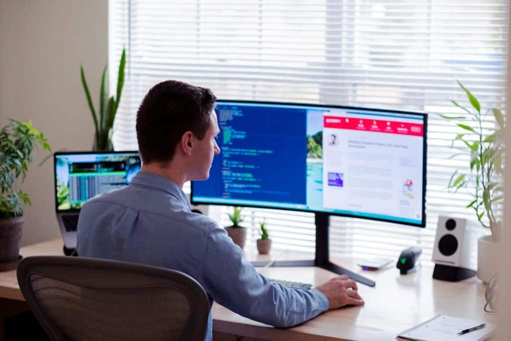 Professional using dual monitor setup to work with business software applications in modern office environment with natural lighting and plants.