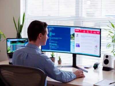 Professional using dual monitor setup to work with business software applications in modern office environment with natural lighting and plants.