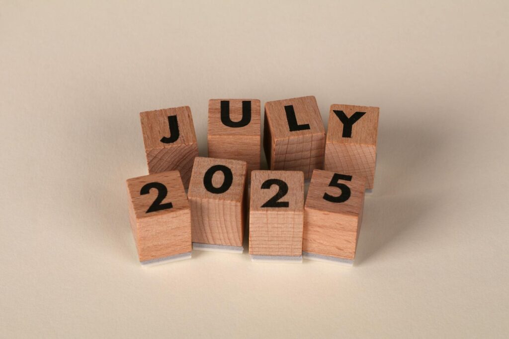 Wooden letter blocks spelling "JULY 2025" arranged in two rows on a neutral background.