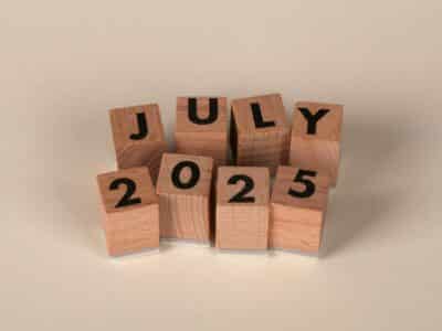 Wooden letter blocks spelling "JULY 2025" arranged in two rows on a neutral background.