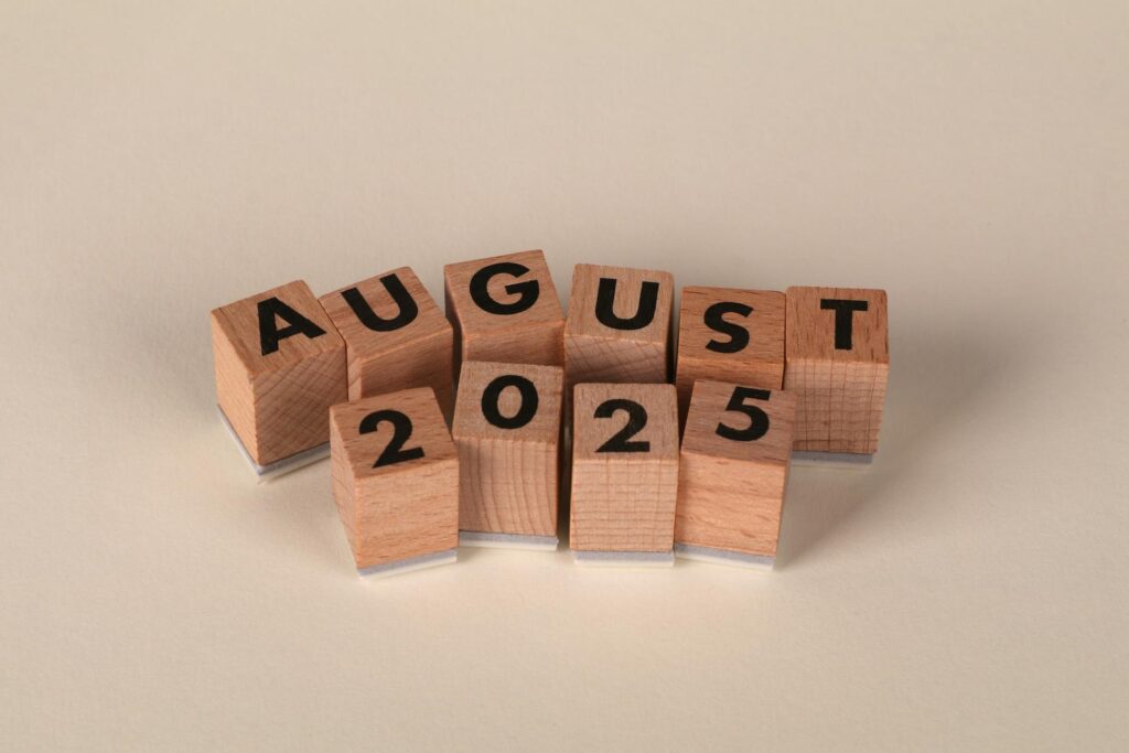 Wooden letter blocks spelling "AUGUST 2025" arranged on neutral background for SWK's cybersecurity news recap article.