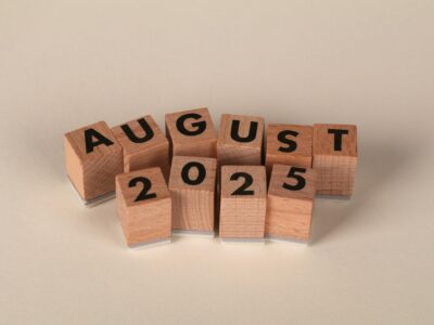 Wooden letter blocks spelling "AUGUST 2025" arranged on neutral background for SWK's cybersecurity news recap article.