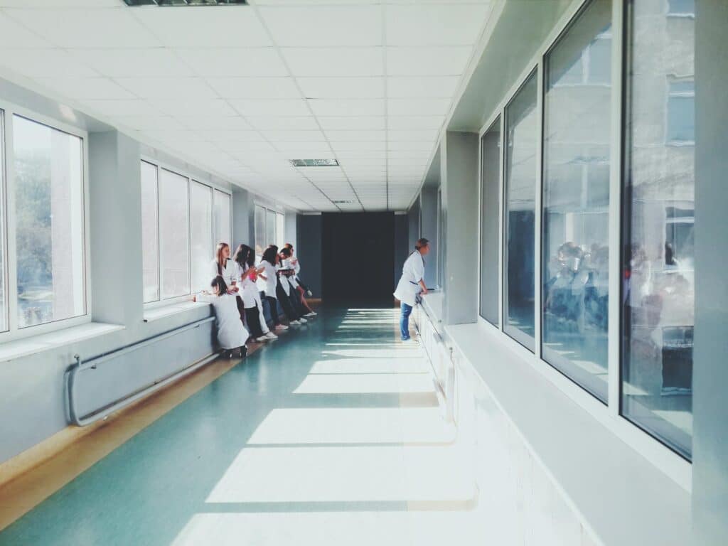Healthcare professionals in white coats gather in a modern hospital corridor with large windows, illustrating the healthcare workforce environment where IT support challenges occur.