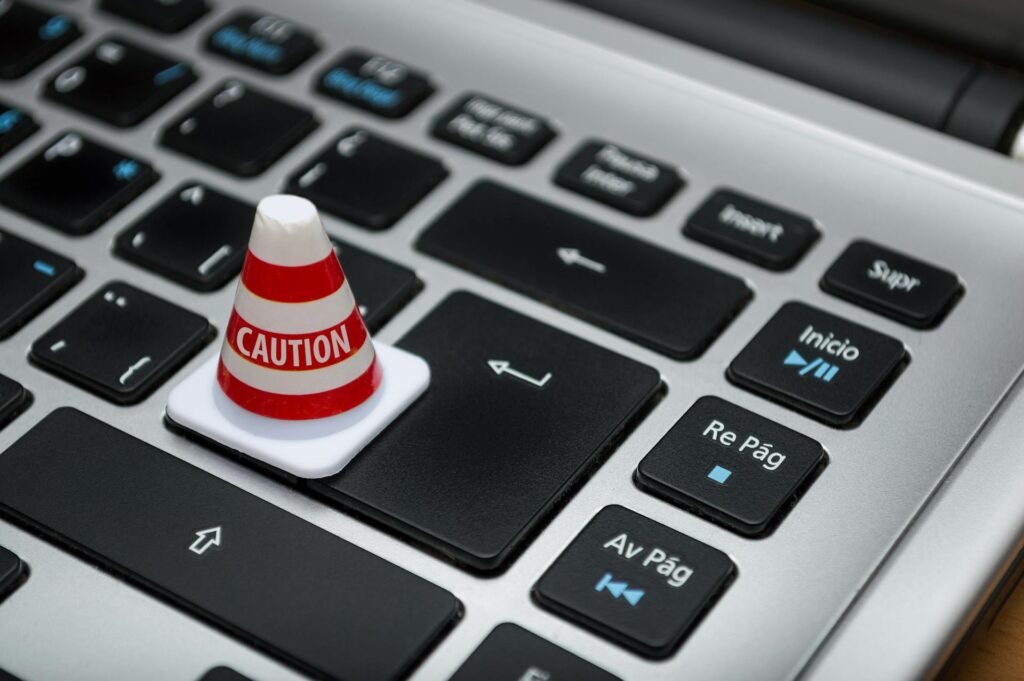 Red and white traffic cone labeled "CAUTION" placed on laptop keyboard keys, representing cybersecurity warnings and security vulnerabilities in on-premise ERP systems.