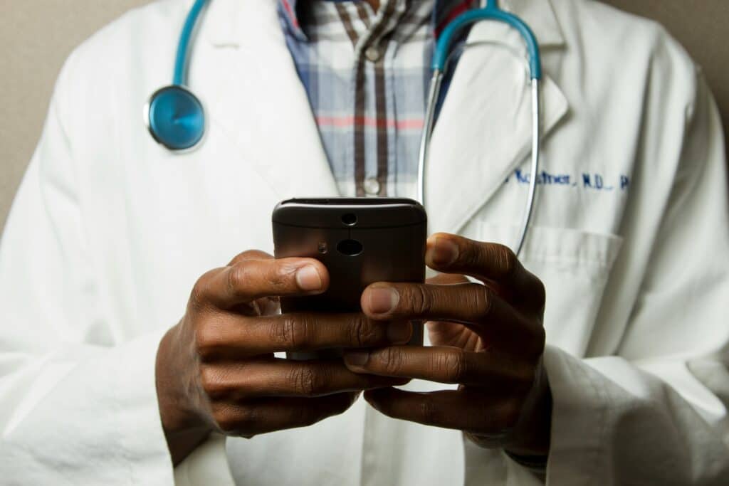 Healthcare professional in white coat with stethoscope using mobile device to access IT systems