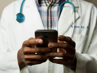 Healthcare professional in white coat with stethoscope using mobile device to access IT systems