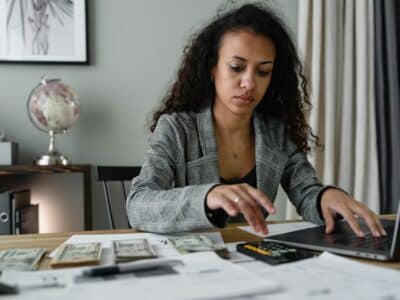 HR professional working on year-end payroll calculations at desk with laptop, calculator and financial documents for Sage HRMS processing.