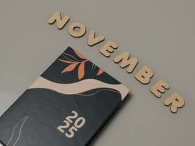 Wooden letters spelling "November" arranged in an arc above a dark notebook with abstract floral design and "2025" on the cover
