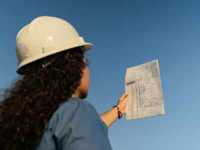 Construction project manager in hard hat reviewing architectural blueprints outdoors, representing year-end project documentation and accounting processes.