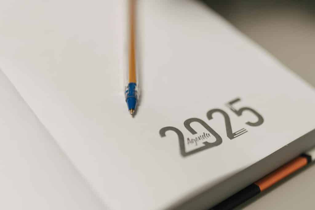 A notebook opened to a blank page marked "2025" with a pen placed across it, representing preparation for Sage 100 year-end closing procedures and tax reporting for the upcoming fiscal year.