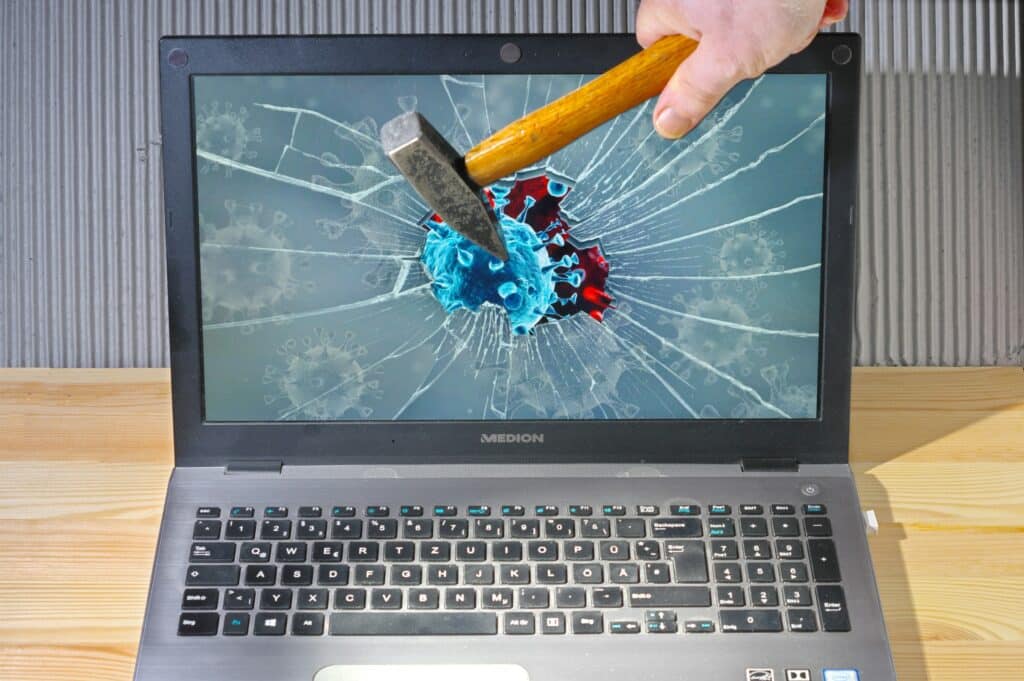 Hammer breaking laptop screen displaying virus graphic illustrating outdated cybersecurity tools vulnerability