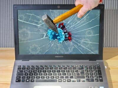 Hammer breaking laptop screen displaying virus graphic illustrating outdated cybersecurity tools vulnerability