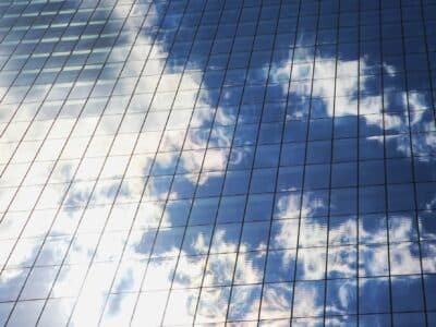 Reflective glass panels on modern office building exterior showing blue sky and white clouds, representing cloud infrastructure technology