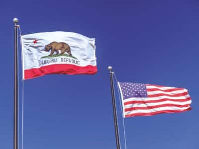 California state flag on the left and United States flag on the right flying side by side on separate poles against a clear blue sky, representing the updates to the CCPA in 2026.