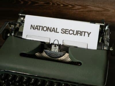 Write Alt Text for this image. 1:50 PM Claude responded: Close-up of a dark green vintage typewriter with a sheet of white paper loaded into the carriage, printed with the words "NATIONAL SECURITY" in bold uppercase … Close-up of a dark green vintage typewriter with a sheet of white paper loaded into the carriage, printed with the words "NATIONAL SECURITY" in bold uppercase black letters, set against a dark wood surface.