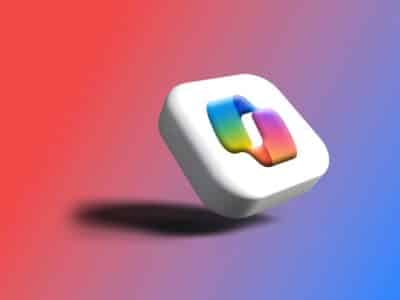 A 3D rendering of the Microsoft 365 Copilot app icon, shown as a white rounded square tilted at an angle with the multicolored Copilot logo on its face, casting a shadow on a red-to-blue gradient background.