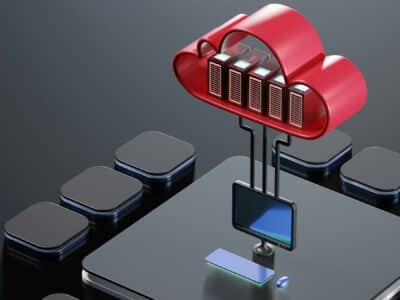 3D illustration of a red cloud icon containing five server racks suspended above a black desktop computer monitor and devices on a dark surface, with cables connecting the servers to the monitor.